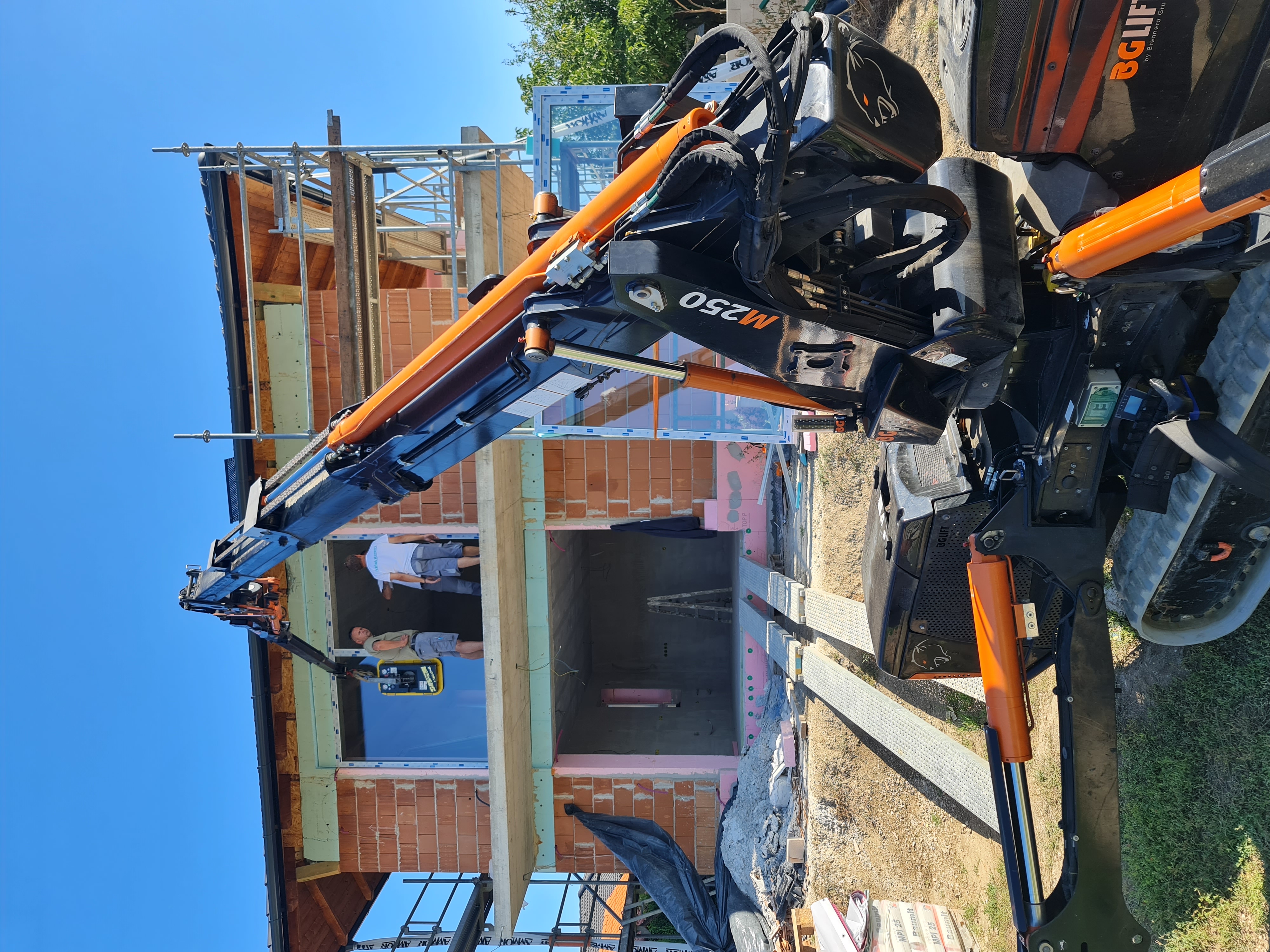 Két emeletes téglaépület építési területe, mini daruval és két munkással a felső szinten.