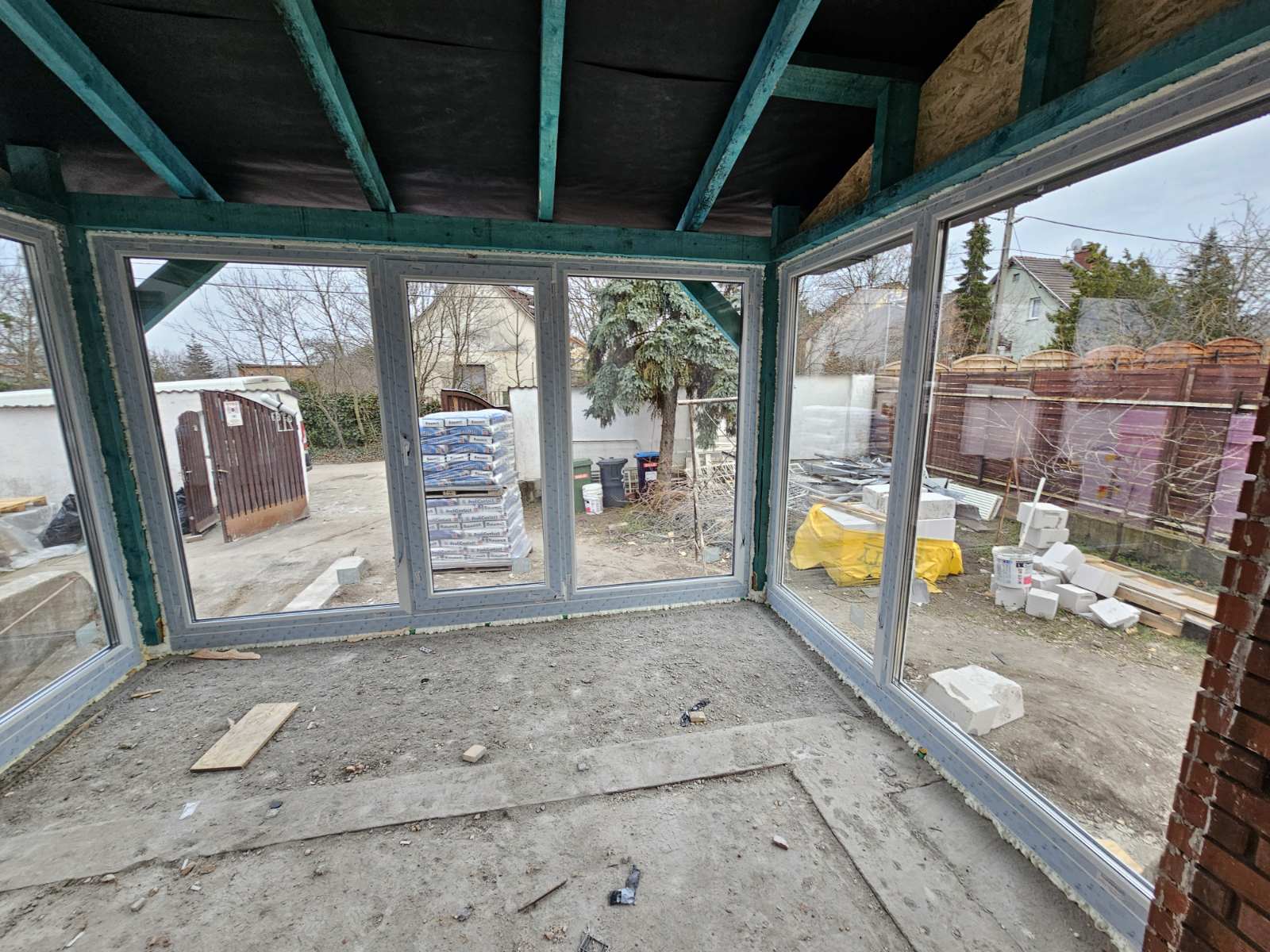 Belső nézet egy épülő télikertről nagy szürke keretes ablakokkal és betonplattal.
