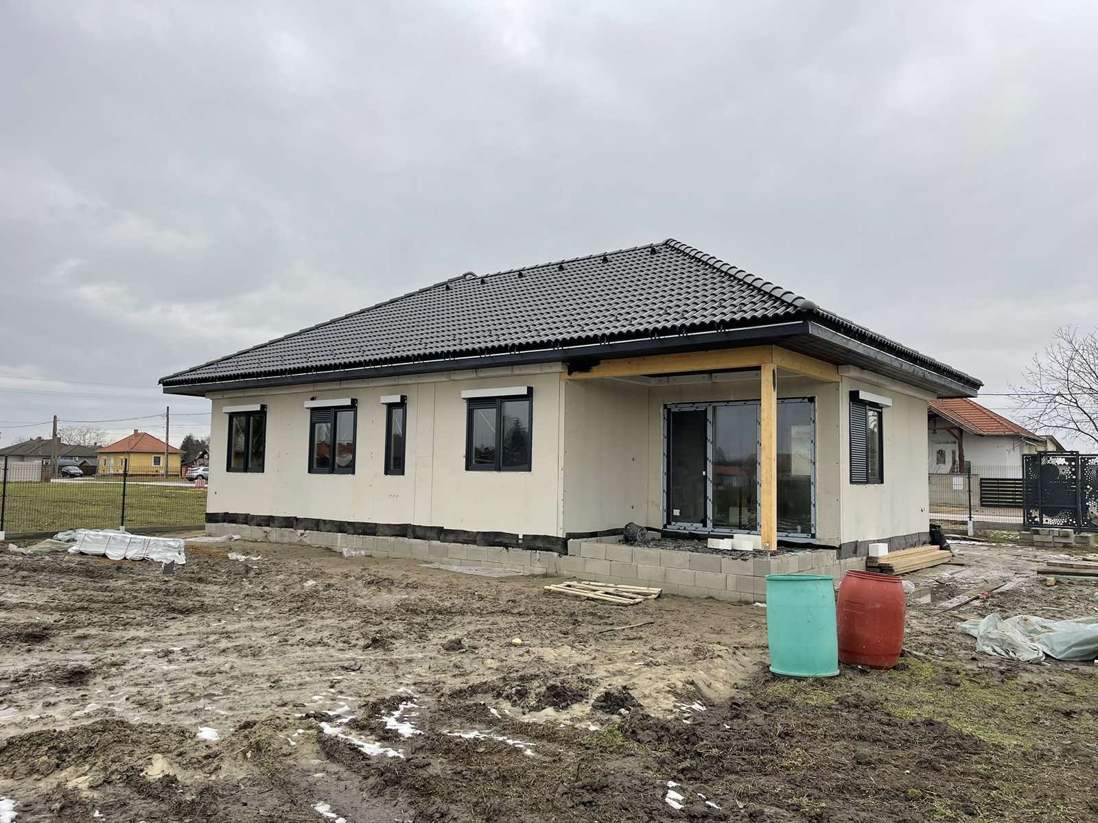 Egy épülő családi ház krém színű falakkal, sötét keretes ablakokkal és cseréptetővel.